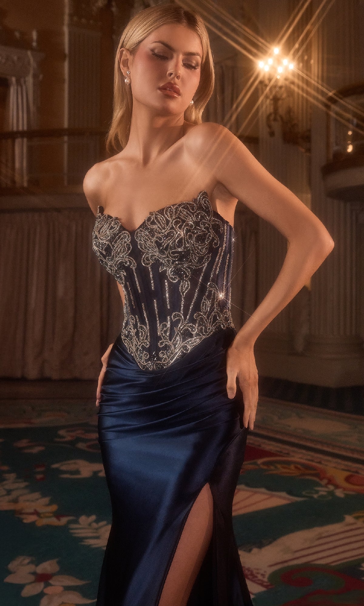 A woman poses indoors under soft lighting, exuding elegance in the navy blue Ladivine CD736 Strapless Long Corset Prom Dress with a beaded bodice and high slit.